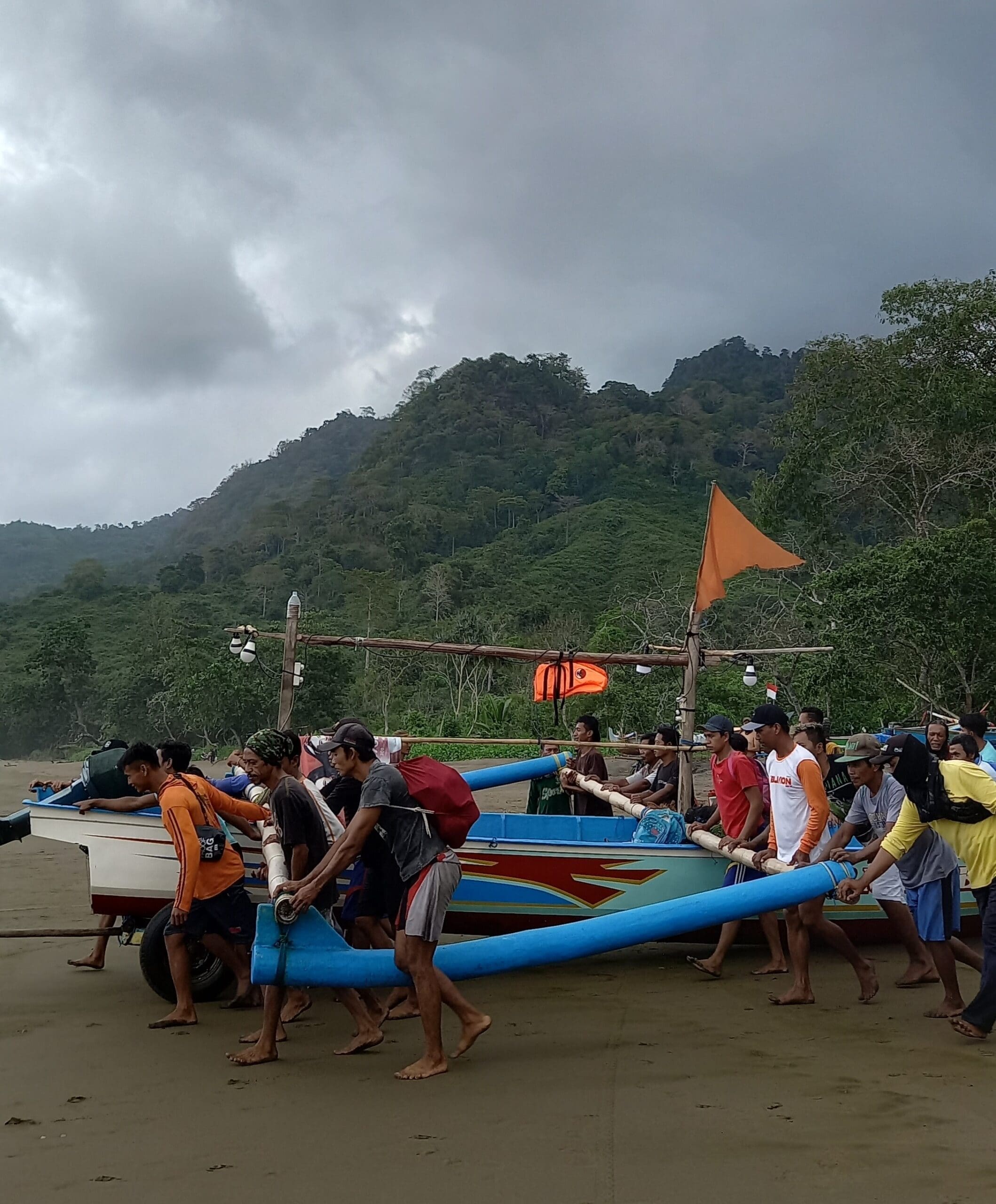 Para nelayan bergotong royong untuk membawa perahu menuju tepi pantai. Sumber: Foto diambil langsung oleh penulis.